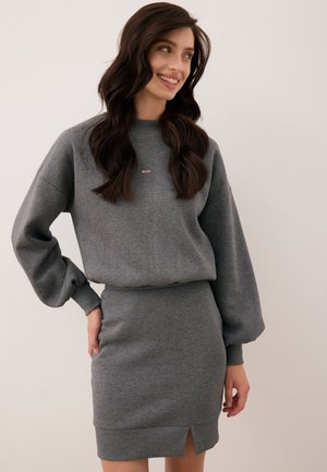 Grijze sweatshirtjurk met een geribde halslijn en ballonmouwen. De rok heeft een zijsplit; de stof lijkt zacht en textuurvol.