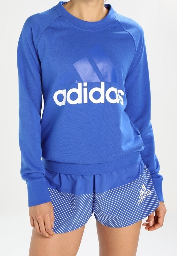 Sudadera azul con logotipo "adidas" blanco; combinada con pantalones cortos a rayas azules. La sudadera tiene un cuello redondo y puños de canalé; los pantalones cortos cuentan con cinturilla elástica.