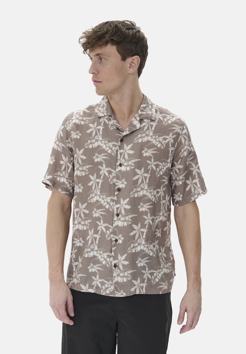 Camisa de manga corta, con botones, en tejido marrón claro con patrones de hojas blancas. Cuenta con un collar tipo camp y un bolsillo en el pecho.