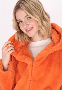Giacca con cappuccio in finta pelliccia arancione brillante, dal tessuto morbido, con zip frontale e dal design oversize accogliente.