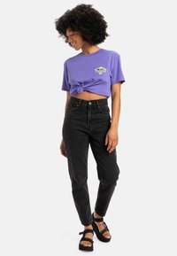 Paarse cropped t-shirt met een knoop aan de voorkant, gecombineerd met hoge zwarte jeans en zwarte sandaaltjes met plateauzolen.