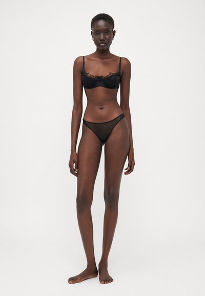Soutien-gorge noir à dentelle et culotte transparente noire, présentant des détails délicats, des bretelles réglables et un design minimaliste. Texture lisse.