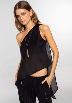 Top nero asimmetrico realizzato in tessuto trasparente, con una spalla e un orlo fluente. Abbinato a pantaloni neri con paillettes.