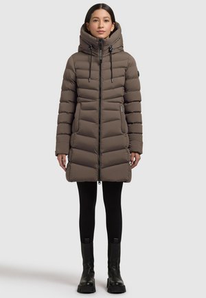 Vadderad parkas i mörk taupe med hög krage, framfickzipp, dragsko i huva och vertikala sömmar. Stylad med svarta leggings och stövlar.