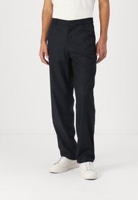 Navy tailored trousers with a straight fit, flat front, single button closure, and side pockets. Paired with white sneakers.