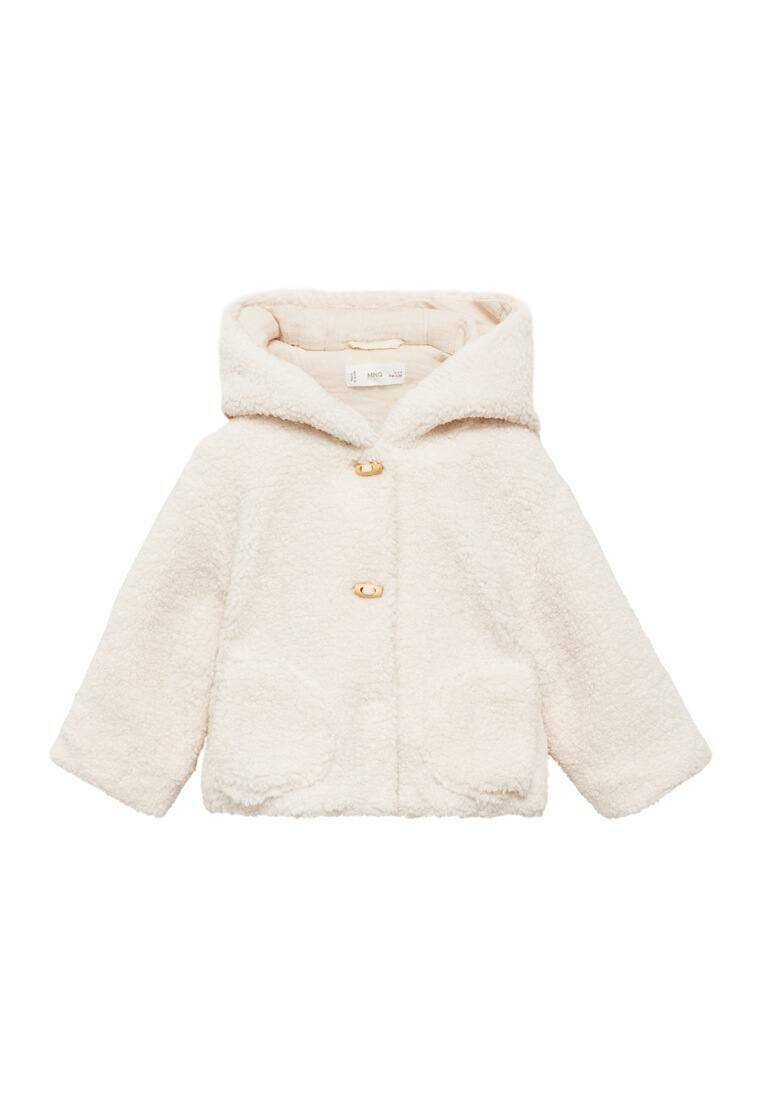 Kremvärinen tekoturkis takki huoodilla, jossa on kaksi etutaskua ja kultaiset napit. Takissa on teksturoitu, pehmeä kangas ja lyhyet hihat.