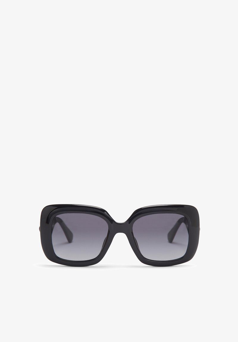 Lunettes de soleil noires oversize avec montures carrées, verres dégradés foncés et finition lisse et brillante. Elles présentent des branches épaisses avec des courbes subtiles.