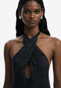 Black halter dress with a keyhole cutout and leafy pattern. The model wears silver floral earrings and has straight, dark hair.