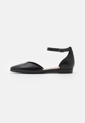 Chaussure plate noire à bout pointu, côté ouvert, talon fermé, et bride de cheville réglable avec boucle sur fond blanc.