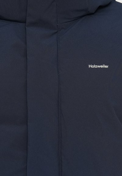 Sodinės mėlynos spalvos švarkas su lygiu paviršiumi, kuriame yra baltu šriftu užrašyta prekės ženklas "Holzweiler". Jis turi užtrauktuko uždarymą ir paminkštintą dizainą.