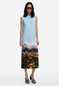 Faltenmidikleid in Hellblau mit einem fotografischen Landschaftsprint, der zu lebendigen orangen Blütendetails am Saum übergeht.