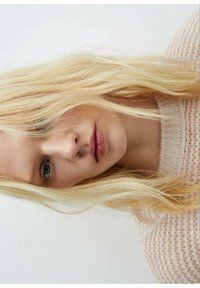 Lähikuva henkil�östä, jolla on pitkät, suorat vaaleat hiukset, pukeutuneena pehmeään, neulottuun, vaaleanväriseen vaatteeseen, jossa on löysä rakenne.