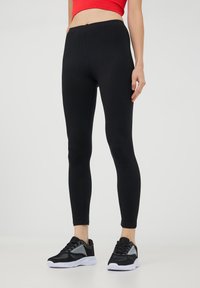 Czarne legginsy wykonane z elastycznego materiału, z dopasowanym krojem i długością do kostek, połączone z czarno-szarymi butami sportowymi.