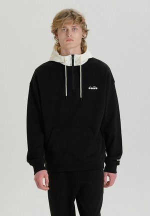 Felpa nera con cappuccio color crema e zip, dotata di una tasca frontale e di un piccolo logo bianco sul petto. Tessuto morbido.