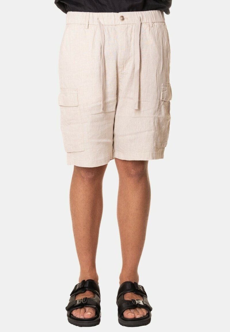 Pantaloni cargo beige chiaro in lino, con vita regolabile con cordino, due tasche laterali e una vestibilità ampia. Abbinati a sandali neri.