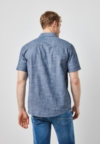 Kortärmad skjorta med knappar i ett ljust blått vävt tyg med en texturerad yta och rundad nederkant. Kombineras med blå denimjeans.