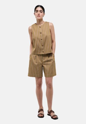 Femme portant un haut sans manches rayé marron à boutons et un short assorti avec poches, associé à des sandales marron, debout devant un fond uni.
