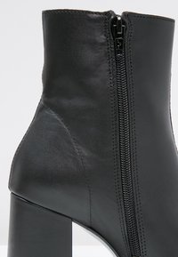 Bottine en cuir noir avec une fermeture éclair latérale et un talon haut épais, présentant des coutures détaillées et une texture lisse.