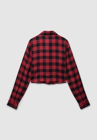Camicetta corta a maniche lunghe a fantasia a scacchi rossa e nera. Realizzata in un tessuto morbido con colletto e polsini abbottonati. Dettagli di cucitura notevoli.