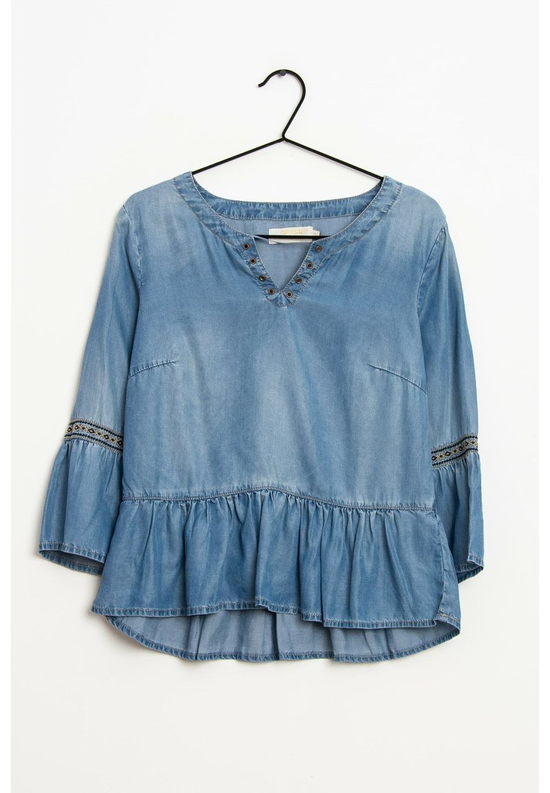 Blouse en denim avec un col en V, des manches évasées trois quarts, un ourlet peplum et des accents brodés. Couleur bleu clair avec une texture douce.