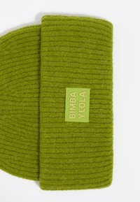 Bufanda de lana verde tejida con una textura acanalada y una etiqueta rectangular de color verde menta con letras en relieve.
