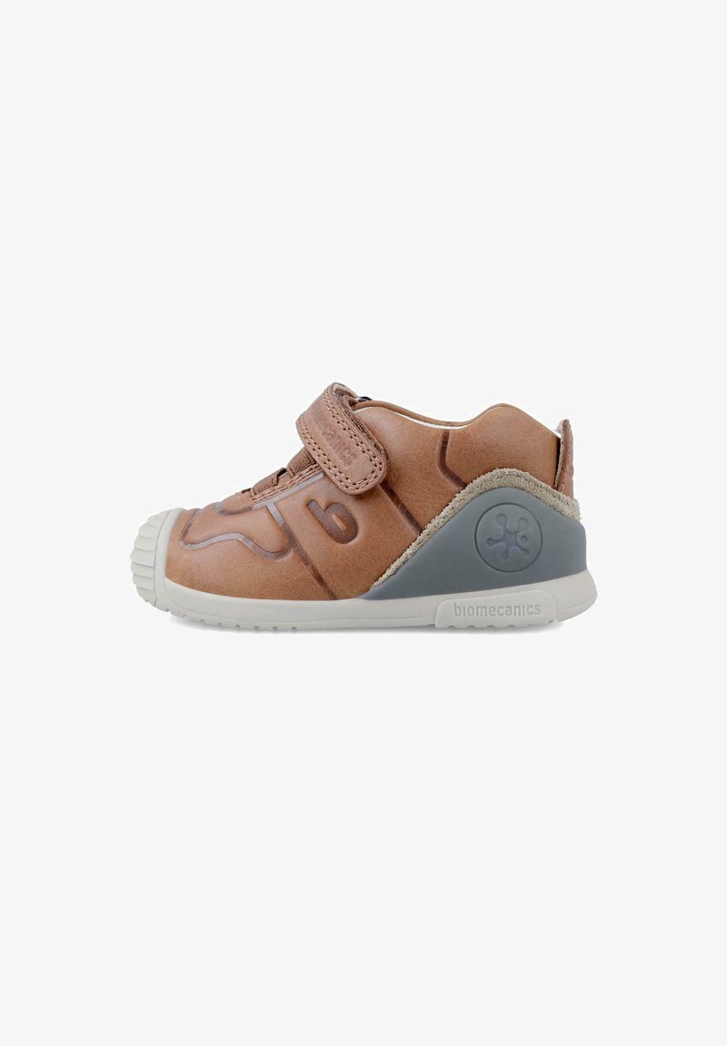 Zapatilla de cuero marrón con una cinta de velcro, suela de goma y suaves acentos grises. Presenta un diseño moldeado en la parte delantera y un logo de marca en el talón.