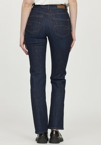 Jean en denim bleu foncé avec une coupe droite, comprenant deux poches arrière et des accents de couture jaune. Texture lisse avec une coupe classique.