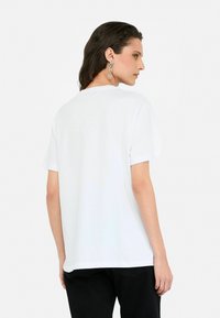 Tricou alb cu mânecă scurtă și guler rotund, având o croială lejeră și o textură netedă, asortat cu pantaloni negri.
