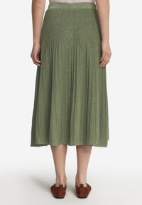 Plisserad midikjol i ljusgrön med subtil lyster, strukturerad tyg, elastisk midja och bruna ballerina-skor synliga vid nederdelen.