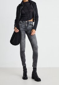 Chaqueta de cuero negra, top texturizado gris, jeans gris ajustados y botas de tobillo de plataforma negras. Sostiene un bolso negro texturizado.