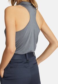 Haut sans manches gris avec un encolure ronde et une découpe au dos, associé à un pantalon noir délavé ajusté avec poches et accents de boutons.