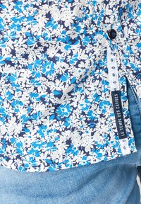 Camicia a maniche corte floreale in blu navy con fiori bianchi e blu, dotata di etichetta "LE TEMPS DES CERISES" e dettaglio dei bottoni sul lato.