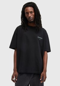 Juodas medvilninis per didelis t-shirt su trumpomis rankovėmis, su baltu "ALLSAINTS" logotipu ir minimalistiniu dizainu, lygia tekstūra.