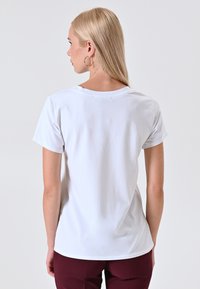 T-shirt bianca a maniche corte con scollatura rotonda, realizzata in tessuto morbido, caratterizzata da un orlo curvo e priva di motivi o grafiche visibili.