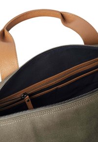 Sac en toile avec un intérieur sombre, des poignées en cuir beige et un compartiment zippé avec des fermetures éclair marron et des poches supplémentaires.