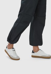 Vita sneakers med grå mockadetaljer och svart häl detalj. Snörningsdesign med gummisulor. Bärs tillsammans med mörka, tapered cargo-byxor.