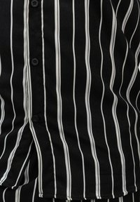 Tissu rayé noir et blanc avec une texture légère, comportant une fermeture à boutons sur le devant et un motif de rayures verticales.