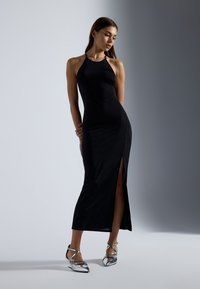 Crna halter haljina s bočnim prorezom; elegantan dizajn i glatka tekstura. Uparena sa srebrnim ravnim sandalama s izduženim vrhom.