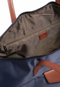 Tote bag en tissu marine à l'intérieur avec une doublure en tan lisse, comportant une poche zippée et une étiquette de marque en cuir. Accents de sangle en cuir marron.