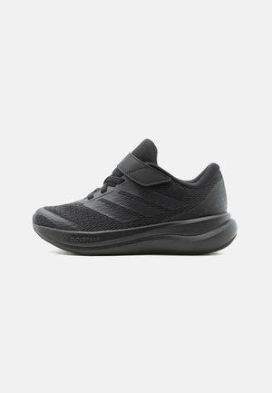 Czarny sportowy sneaker z siateczkową cholewką, paskiem na rzep oraz wyściełaną podeszwą, przedstawiony w widoku bocznym na białym tle.