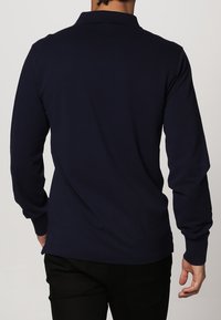 Marineblaues Langarm-Polohemd mit Kragen und geknöpften Ärmeln. Glatte Stoffstruktur, taillierte Form und gerader Saum. Rückansicht gezeigt.