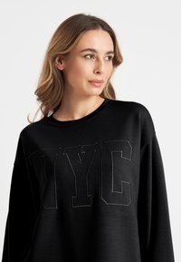 Zwarte sweatshirt met grote "NYC" letters op de voorkant in een textuurafwerking. Ronde halslijn, losse pasvorm en zachte stof.