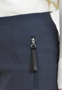 Marineblauwe broek met een zijritszak en een zwart trekband, gemaakt van een gladde stof met een getailleerde pasvorm.