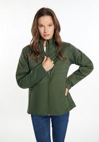 Grüne Puffjacke mit hohem Kragen, Reißverschluss und seitlichen Taschen. Glattes Gewebe mit gestepptem Muster; getragen mit Jeanshosen.