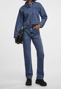 Jeansjacka och jeans i medelblå tvätt, med en kortad design, knäppningar, sidofickor och matchat med svart väska och skor.