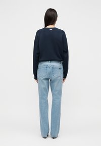 Tamsiai mėlynas džemperis su apvalia iškirpte, laisvo stiliaus ir nuleistais pečiais, derinamas su šviesiai mėlynais tiesiais džinsais, turinčiais galines kišenes.