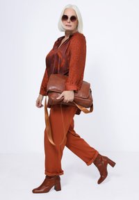 Braune Leder-Umhängetasche, rostfarbener Bluse mit Muster, passende schmal geschnittene Hose und braune Absatz-Ankle Boots. Rund Sonnenbrille.