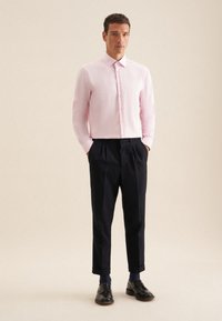 Camicia button-up rosa chiaro con maniche lunghe, abbinata a pantaloni blu navy. Scarpe nere completano il look, mostrando un design classico e su misura.