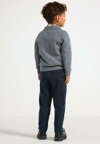 Grå uldtrøje med krave, kombineret med mørkeblå bukser. Outfittet har en diskret tekstur og sorte sko med en kraftig sål.