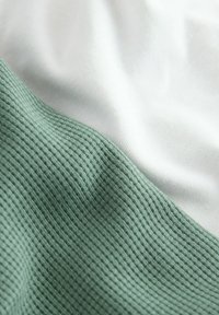 Tekstil med en tekstureret grøn sektion med lodrette ribber og en glat hvid sektion, der fremhæver kontrasterende materialer og farver.